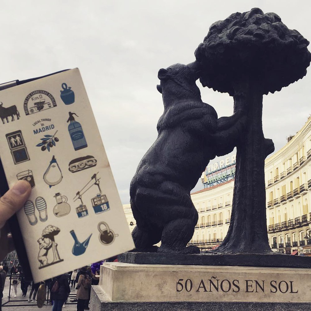 Traveler holding a Madrid travel journal in front of the Bear and Strawberry Tree statue
